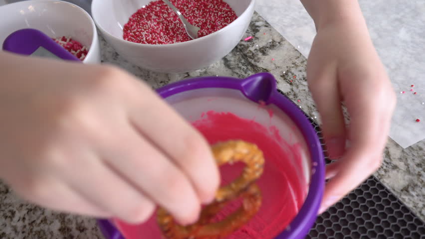 With focused attention, this budding culinary artist dips pretzels into a pot of melted chocolate, creating sweet delights in the warmth of a well-lit home kitchen.
