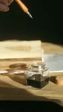 Close up writer hand dipping classic wooden dip pen with metal nib into glass inkwell of black ink preparing to write on aged paper in warm natural sunlight. Calligrapher dipping vintage pen. Vertical - Powered by Shutterstock - Get 15% off with code: PIKWIZARD15