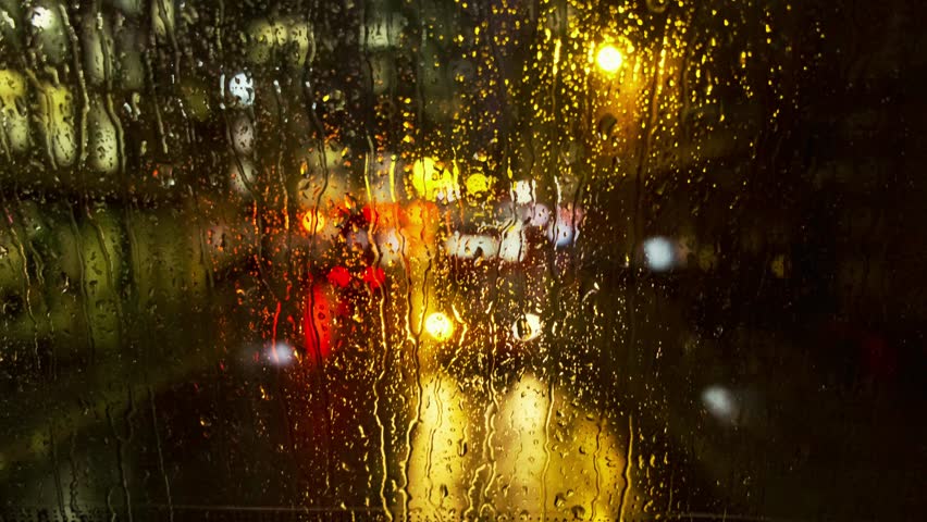 The view from inside a London bus on a rainy night. Rivulets of rain stream down the back window, transforming the glowing red taillights and traffic of the city into a beautiful motion and colour.