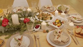A detailed 4K video showing a beautifully decorated table set for a festive holiday meal, featuring a lush centerpiece of fir, eucalyptus, white berries, pomegranates, and warm ambient candlelight. - Powered by Shutterstock - Get 15% off with code: PIKWIZARD15