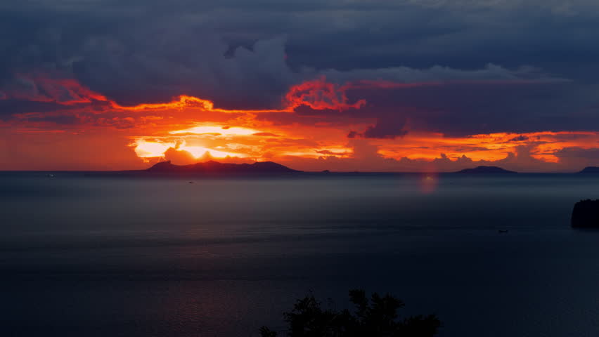 Close-Up of Ocean Horizon with Glowing Orange Sky at Sunset and Dark Clouds Over Island Silhouettes, Peaceful Evening Concept.