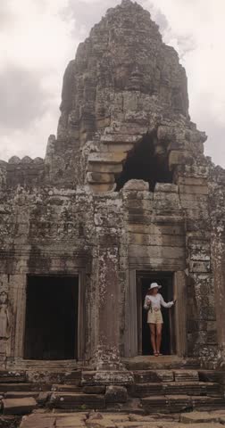 Young woman traveler with hat and backpack exploring the entrance of Bayon Temple in Angkor Thom, Cambodia. High quality conceptual footage for tourism, history, adventure, and cultural heritage promo