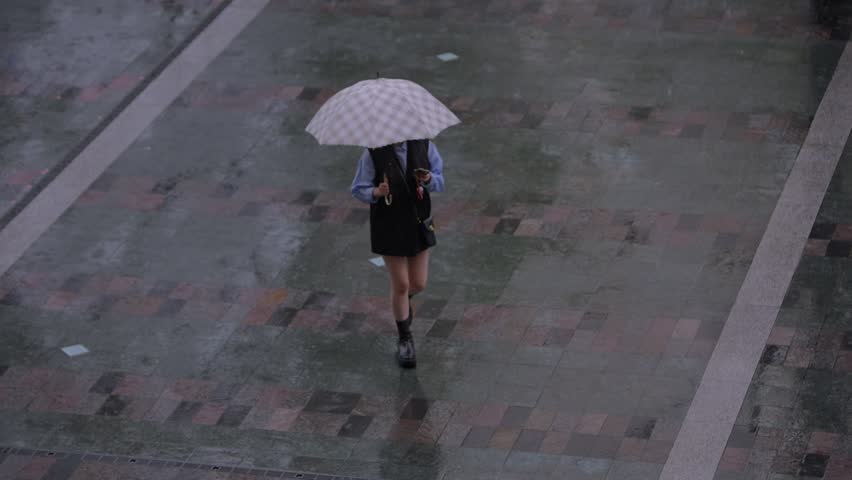 Slow motion showing a lone person walking with an umbrella across a wet stone street near Hakata Station in Fukuoka, Japan, with gentle reflections on the pavement