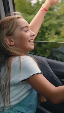Lovely satisfied carefree 12-year-old girl rejoicing about good weather,the light breeze blowing on her hair through open window while she driving on the car