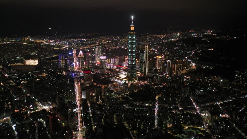 Aerial footage over Taipei at night, vibrant capital of Taiwan, with landmark 101 Tower amid skyscrapers in Xinyi Financial District, crowded buildings in downtown and dazzling city lights in the dark