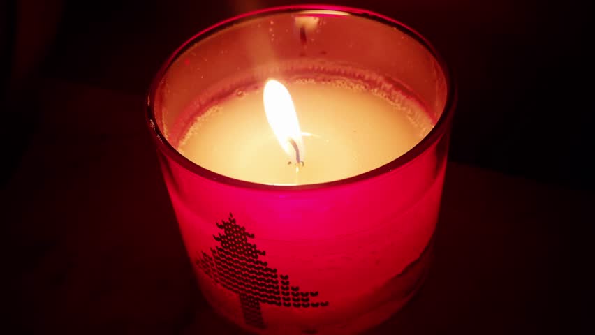 A festive Christmas candle glowing warmly inside a red glass holder with a holiday tree pattern - Powered by Shutterstock - Get 15% off with code: PIKWIZARD15