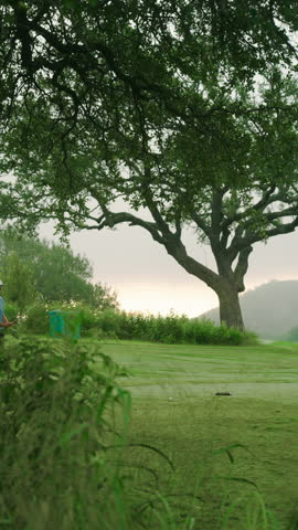 Vertical view of male golfer taking an iron tee shot through tall grasses on fairway. Highlights technique, stance, and scenic course perspective