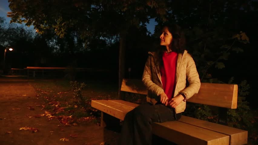 People sitting on the bench in the park at night. Woman relaxing near the river under blue evening sky and street lamp