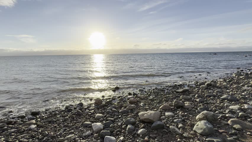 Sunset at the beach in Nova Scotia, Canada on a warm autumn evening while the sun sets in the background. Small rocks lay on the ground and touch the calm water.