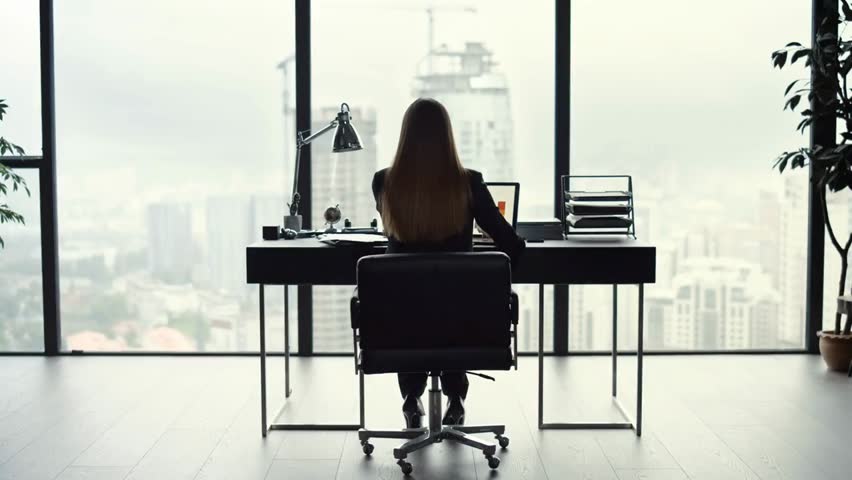 Back view of a businesswoman analyzing graphs on a laptop at a home office, showcasing remote work, entrepreneurship, and professional productivity.