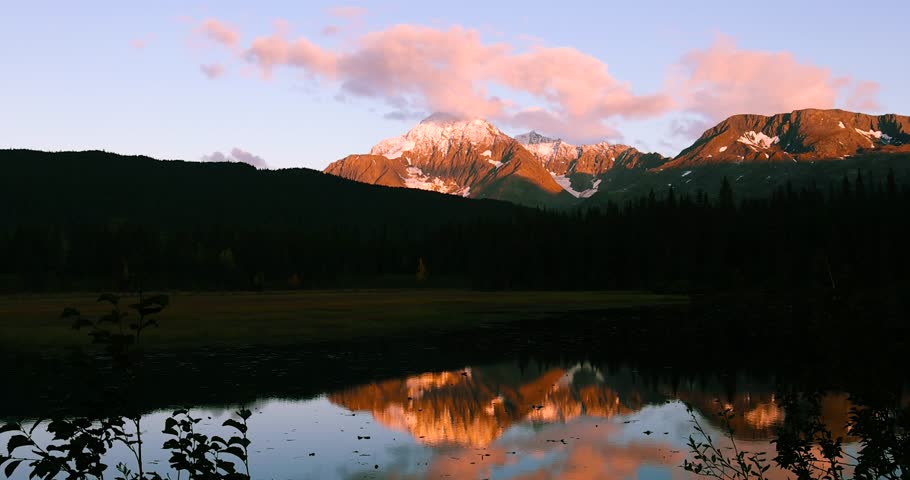 Vibrant lighting on the mountains of Alaskda during twilight, with reflections in lower Trail lake .