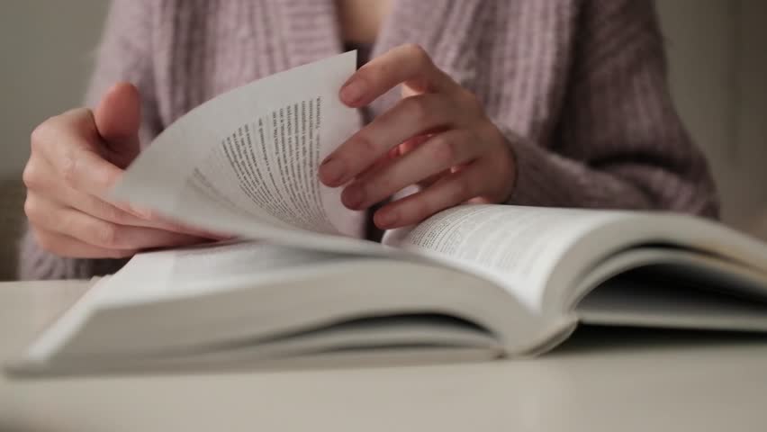 Woman reading an old book. Flipping and old book with stained pages. Flicking through an old textbook closeup, macro shot of paper in university library. Reading and education concept.