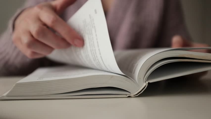 Woman reading an old book. Flipping and old book with stained pages. Flicking through an old textbook closeup, macro shot of paper in university library. Reading and education concept.