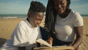 African american mother and son relax on sunlit beach, sharing storybook and smiling as they bond over reading, learning and family time during a seaside vacation - Powered by Shutterstock - Get 15% off with code: PIKWIZARD15