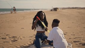 Joyful african american sister and her younger brother having fun together, blowing large soap bubbles on a sunny beach while enjoying a beautiful summer day by the ocean - Powered by Shutterstock - Get 15% off with code: PIKWIZARD15