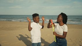 Happy african american mother and her joyful son enjoy family picnic on sunny beach by ocean, playing and blowing bubbles on perfect day - Powered by Shutterstock - Get 15% off with code: PIKWIZARD15