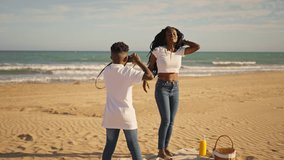 Joyful african american woman with long braids dancing and posing happily while young boy takes pictures with vintage camera during sunny day picnic on sandy beach - Powered by Shutterstock - Get 15% off with code: PIKWIZARD15