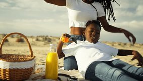 Happy african american mother and cheerful son having fun on beach picnic, playing with oranges and taking selfie together while enjoying their quality family time outdoors on sunny day - Powered by Shutterstock - Get 15% off with code: PIKWIZARD15