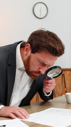 Middle-aged businessman at home office reads contract small text with magnifier finds error and shakes head no. Freelancer guy at table writes urgent fix on sticker and sets note for update this time.