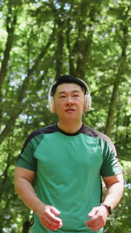 Athletic fitness sport runner man training marathon run, listening music in headphones. Workout cardio outside in park at morning. Asian young man enjoying healthy lifestyle. Active sportsman jogger.