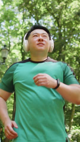 Athletic fitness sport runner man training marathon run, listening music in headphones. Workout cardio outside in park at morning. Asian young man enjoying healthy lifestyle. Active sportsman jogger.