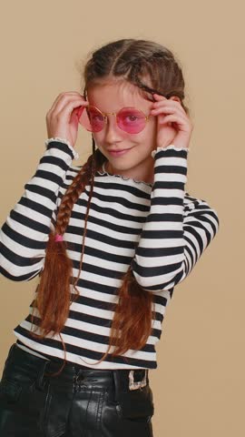 Portrait of happy stylish young preteen child girl kid wearing sunglasses, charming smile, flirting, feeling very proud. Teenager children isolated on beige background indoors. People emotions concept