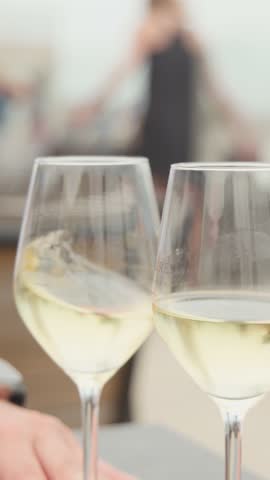 Two hands clink white wine glasses outdoors, soft daylight, shallow focus, relaxed coastal cafÃ© setting