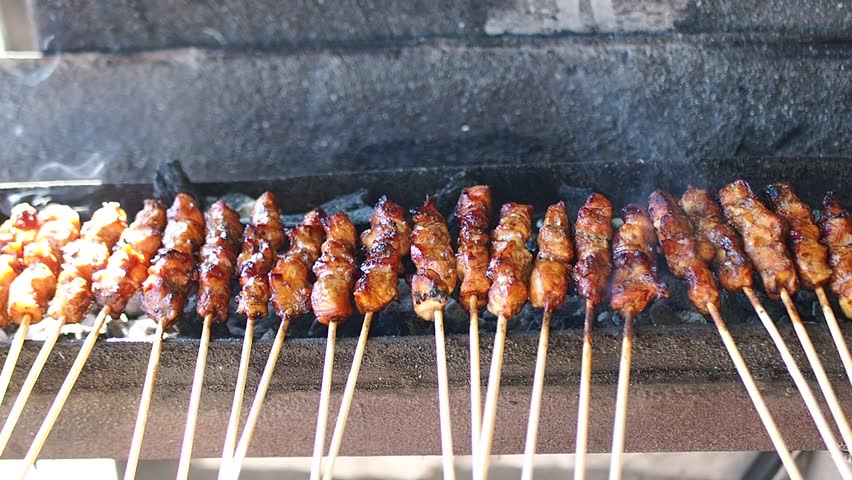 Grilled Indonesian chicken satay (sate ayam) skewers cooking over hot charcoal fire with smoke, a popular street food dish.


