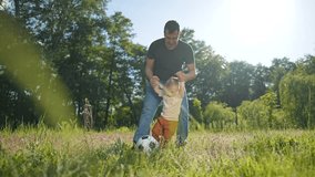 Father bends helping son on field. Son focuses on ball while father holds small hands. Happy summer outdoor scene child and father bonding over soccer. Father, son, ball create playful field energy. - Powered by Shutterstock - Get 15% off with code: PIKWIZARD15