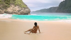 Slow-motion shot of a woman relaxing on wet sand as turquoise waves roll in at Kelingking Beach, Nusa Penida, Bali, ideal for travel promos, wellness branding, social media and luxury beach lifestyle - Powered by Shutterstock - Get 15% off with code: PIKWIZARD15