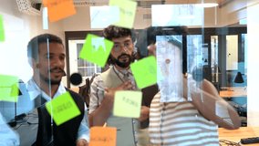 Young diverse creative business team discussing a new project, collaborating, and brainstorming ideas using colorful sticky notes on a glass wall in a modern office or coworking space - Powered by Shutterstock - Get 15% off with code: PIKWIZARD15