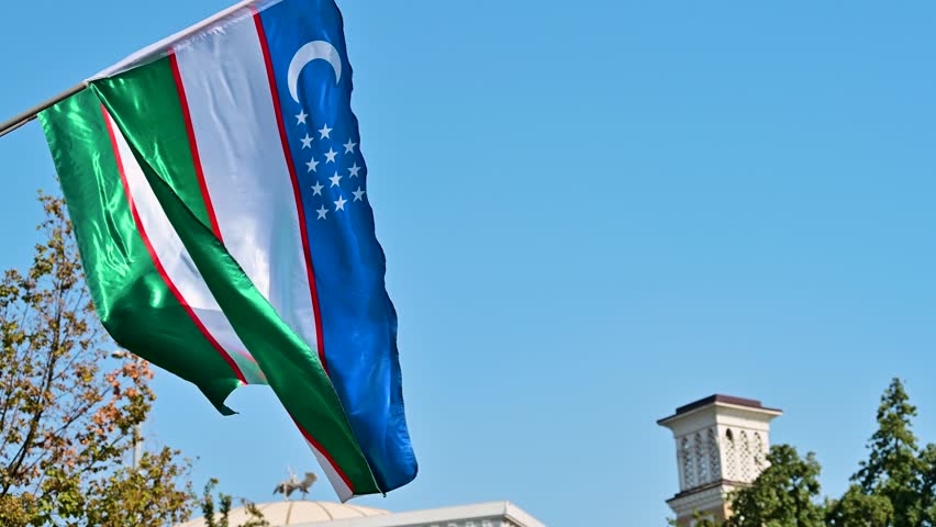 Uzbekistan national flag moving gently in the wind against the sky in Tashkent. Bright colors and clean motion capturing a simple patriotic scene.
