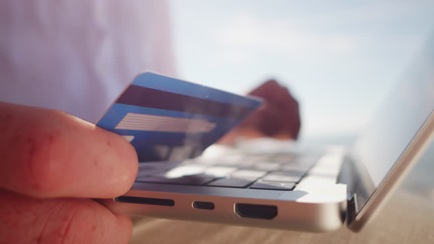 A digital nomad holds a credit card near a laptop, symbolizing remote work and financial transactions. The bright, open environment emphasizes freedom and flexibility in a modern workspace. - Powered by Shutterstock - Get 15% off with code: PIKWIZARD15