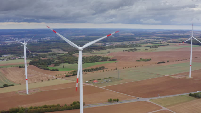 High Quality aerial view of wide fields with tall wind turbines above autumn trees calm sky renewable energy landscape in Luxembourg clean light soft colors and a peaceful cinematic atmosphere.