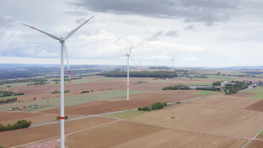 High Quality aerial view of wide fields with tall wind turbines above autumn trees calm sky renewable energy landscape in Luxembourg clean light soft colors and a peaceful cinematic atmosphere.