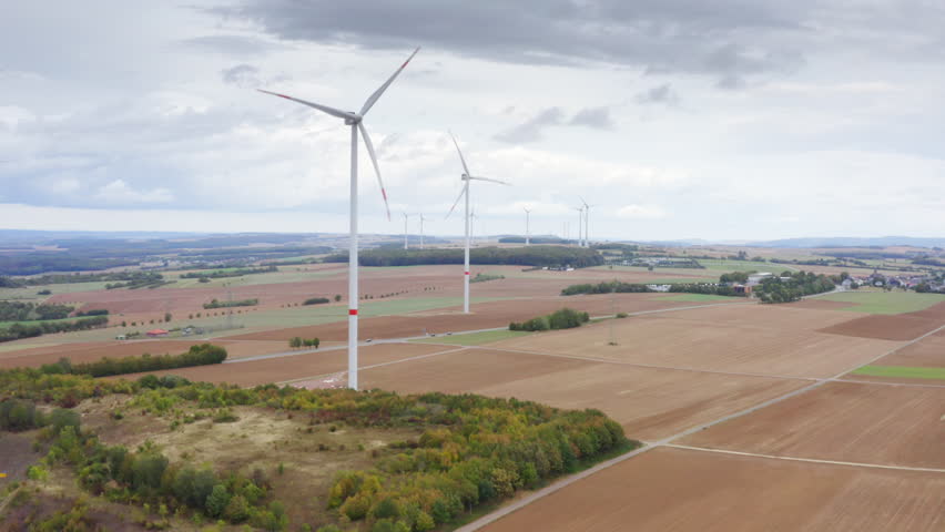 High Quality aerial view of wide fields with tall wind turbines above autumn trees calm sky renewable energy landscape in Luxembourg clean light soft colors and a peaceful cinematic atmosphere.
