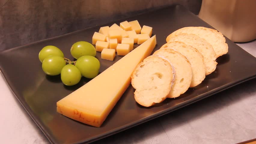 Close-up video of a parmesan cheese platter with grapes and sliced bread on a black plate, filmed with sharp forward camera movements for a dynamic and appetizing presentation.
