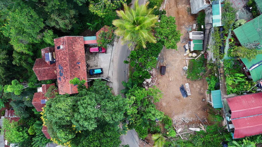 Top-down moving drone shot over a tropical village courtyard with motorbikes, rooftops, and dense greenery in Ella, Sri Lanka.