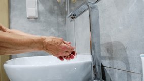 Elderly man stands at modern sink and washes hands carefully. Male washes hands in bright and luxurious bathroom with white marble walls - Powered by Shutterstock - Get 15% off with code: PIKWIZARD15