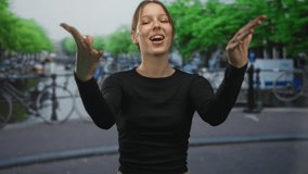 Woman smiling with hand raised in a tossing gesture on a street by an amsterdam canal and bicycles; joyful spontaneity. - Powered by Shutterstock - Get 15% off with code: PIKWIZARD15