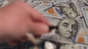 A hand holds a magnifying glass to closely examine the intricate designs of hundred dollar bills placed on a flat surface. - Powered by Shutterstock - Get 15% off with code: PIKWIZARD15