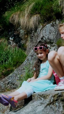 Two pretty girls, kids, sit on a ledge in the rock., a beautiful orange mountain butterfly whirls and flies over a child