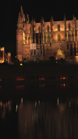 Magnificent Palma Cathedral, also known as La Seu, glowing with golden lights at night, its impressive Gothic architecture beautifully mirrored in the calm waters of the Parc de la Mar below