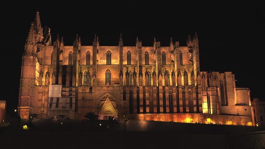The majestic Cathedral of Santa Maria of Palma, known as La Seu, beautifully illuminated at night, with its impressive gothic architecture reflecting on the calm water of the Parc de la Mar