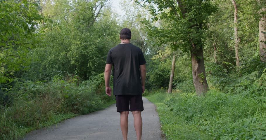 A man walks along path in green spring forest, limping on one leg