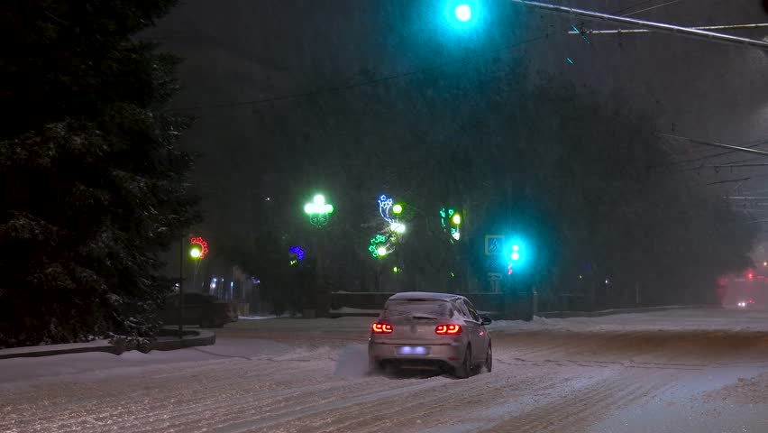 Cars driving along an evening winter city street during a snowstorm. Winter night in the city with snowy street