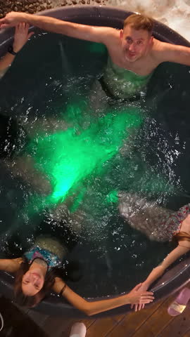 Family of four enjoying a hot tub surrounded by snow on a winter night, Parents with two children relax in an illuminated outdoor hot tub, creating warmth amid the snowy evening