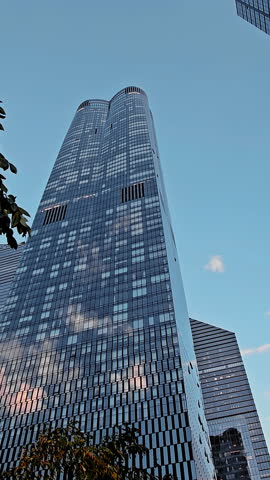 Skyscrapers under a blue sky, modern glass buildings reflecting clouds in a city center.