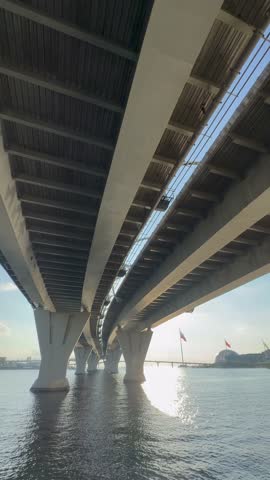 A view of a modern bridge from below, showcasing its structural design and reflections on the water