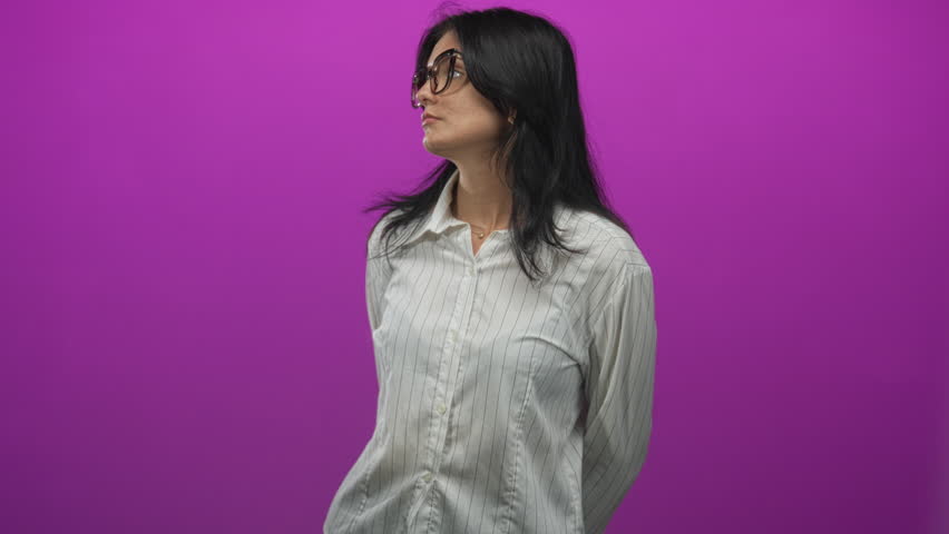 Young hispanic woman wearing striped shirt looks sideways with head tilt at bright purple studio wall; serenity.